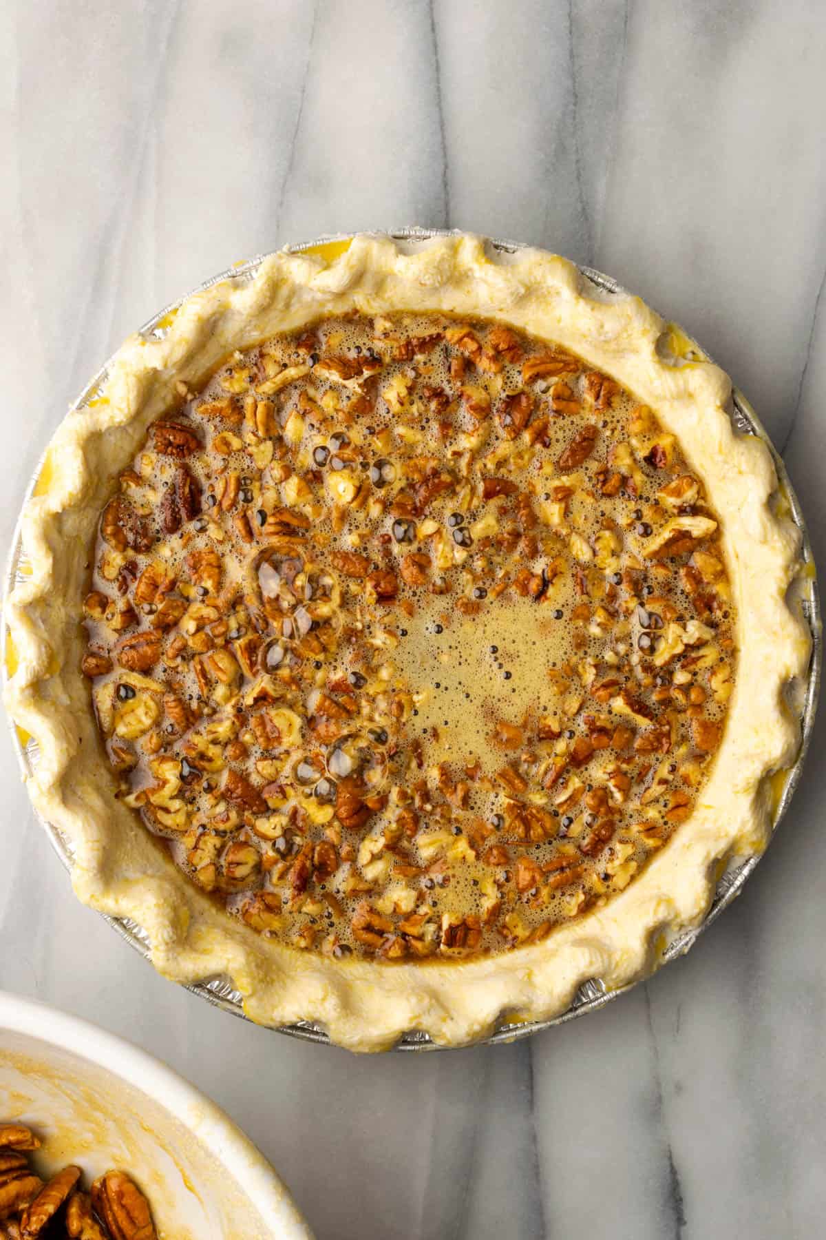 Pecan pie filling and chopped pecans in an unbaked pie shell.