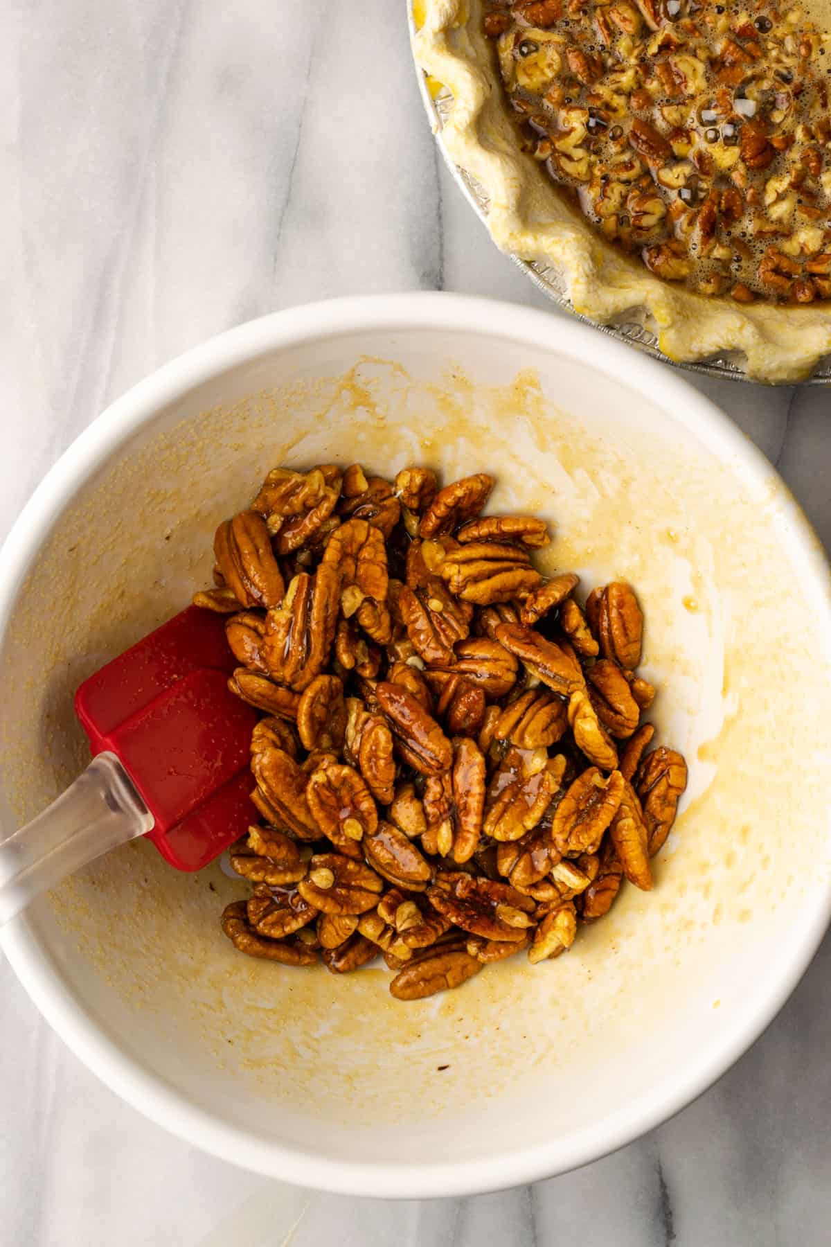 A large white bowl with pecan halves coated in the remaining pie filling liquid.