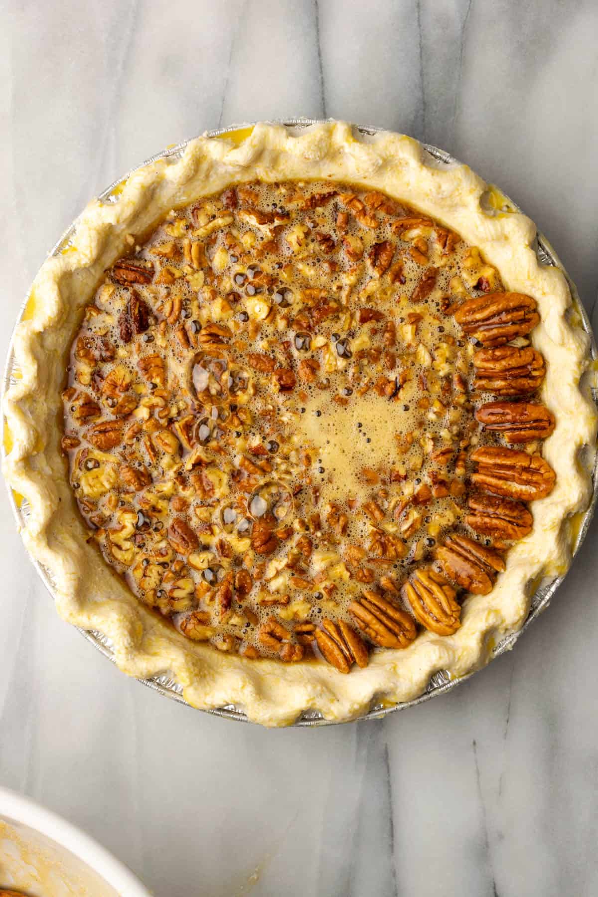 An unbaked pecan pie topped with a row of pecan halves.