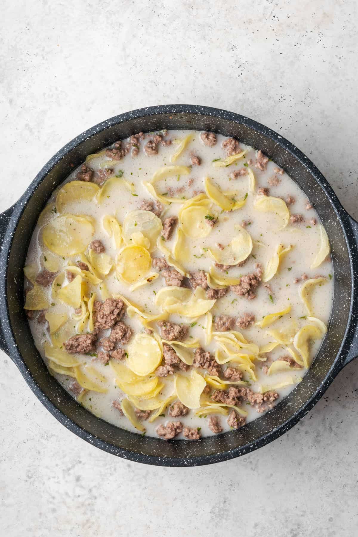 Ground beef, potato slices and liquid in a large skillet.