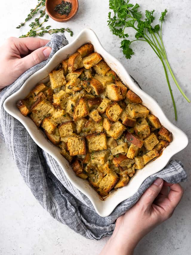 A casserole dish of gluten free stuffing being placed on a white table.