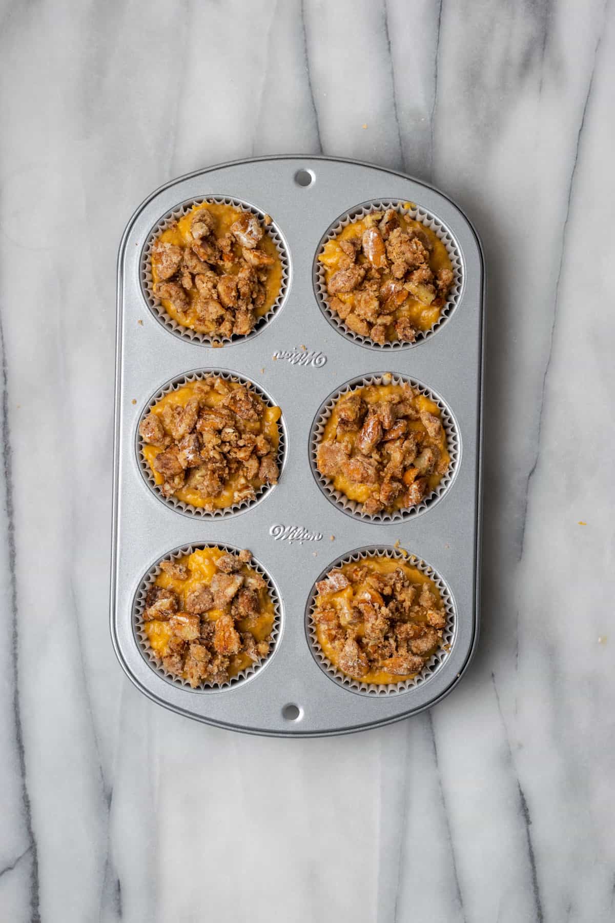 Sweet potato muffins topped with pecan streusel in the metal muffin pan.