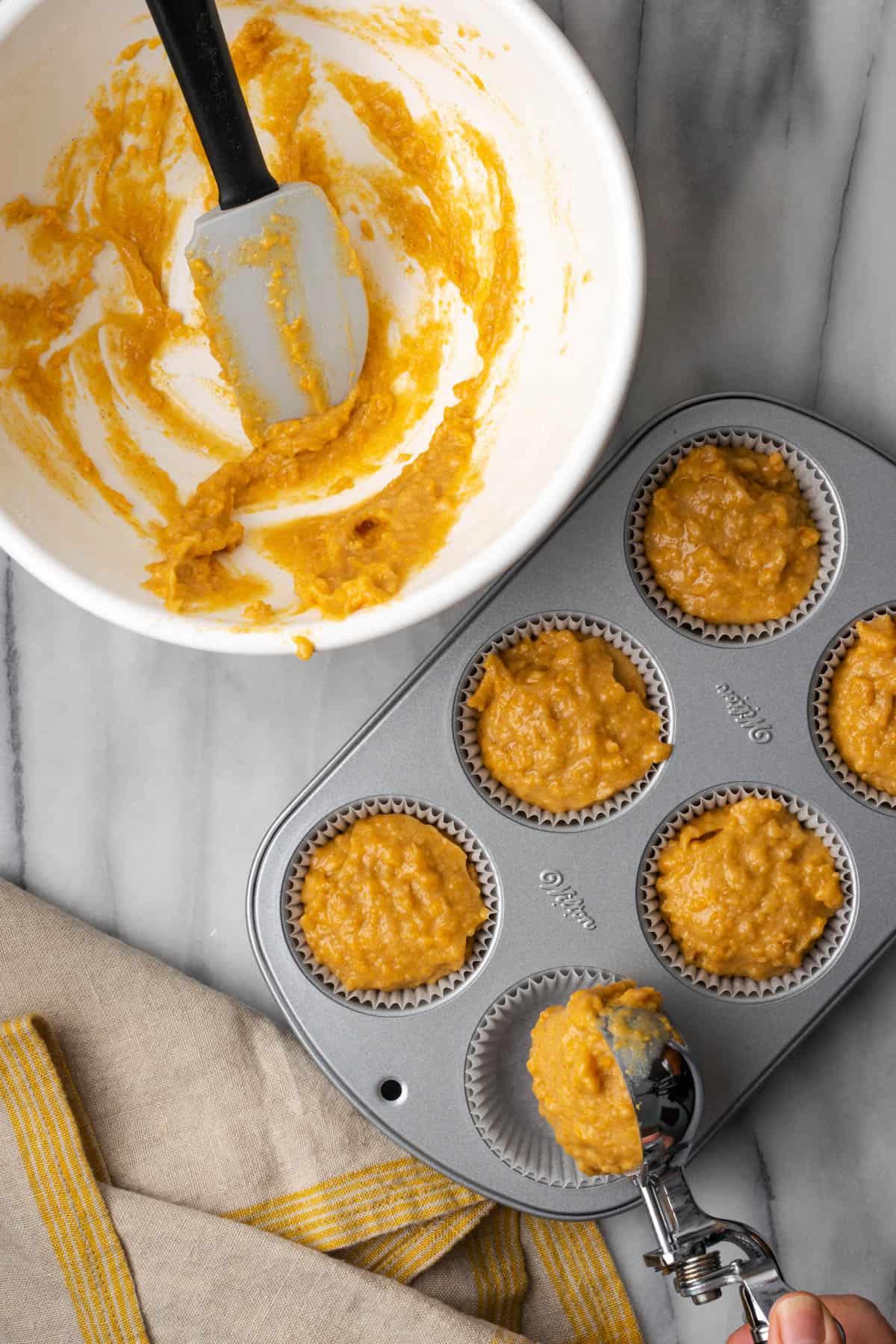 Sweet potato muffin batter being scopped into a metal muffin tin.