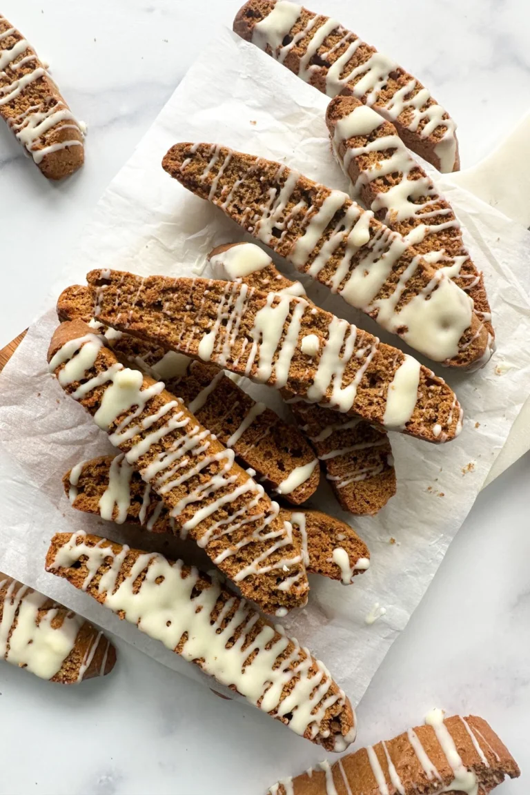 A pile of gluten free gingerbread biscotti coated with a white chocolate drizzle. 