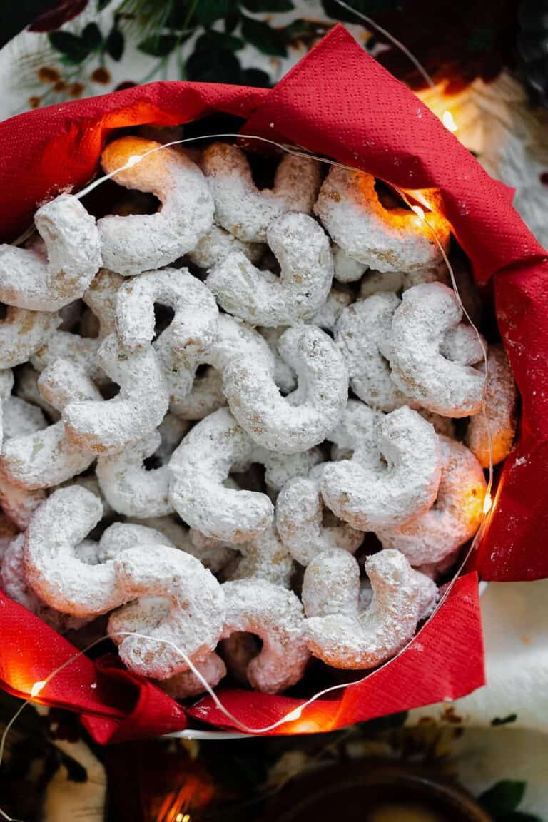 A round tin filled with u-shaped walnut cookies coated in powdered sugar.