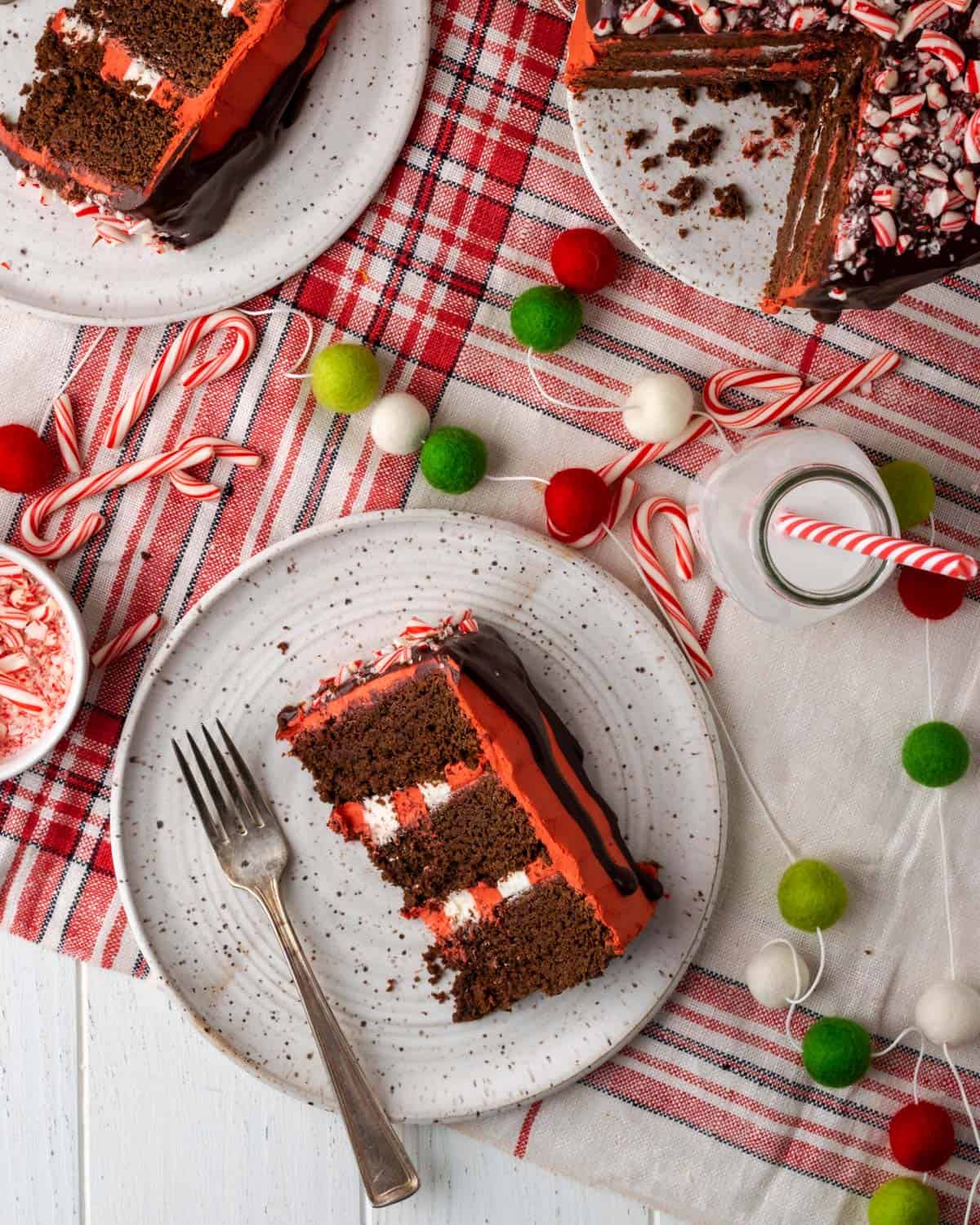Two slices of chocolate peppermint cake on a tabletop decorated with red and green baubles.