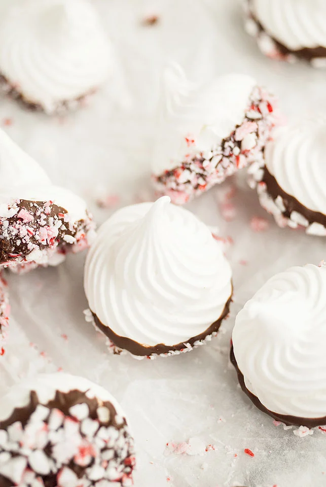 Chocolate dipped peppermint meringue kisses on a white table. 