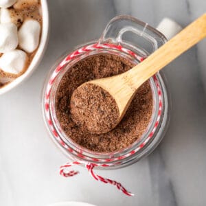 A wooden spoon scooping dairy free hot chocolate mix from a jar.