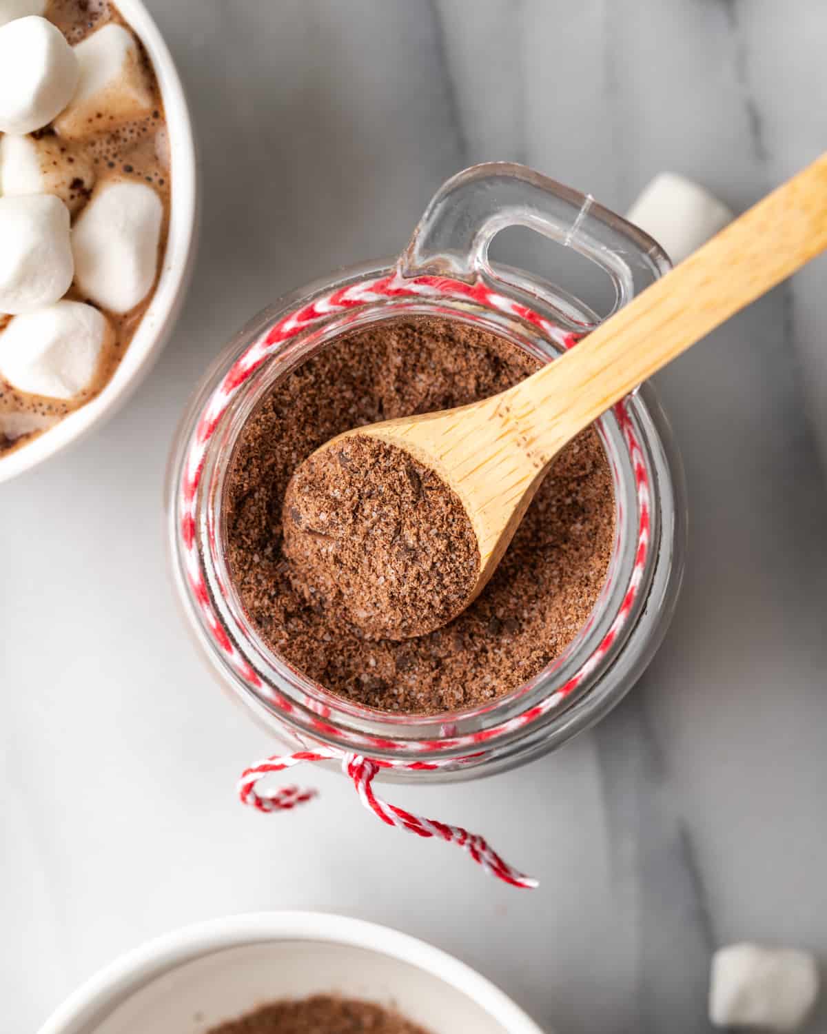 A small wooden spoon scooping hot chocolate mix from a jar.