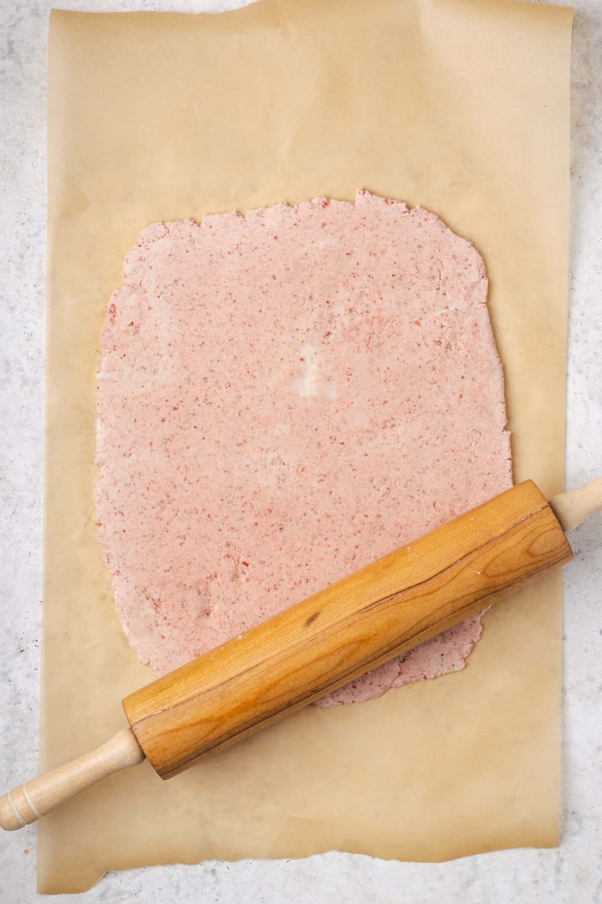Strawberry cheesecake cookie dough being rolled into a large rectangle with a wooden rolling pin.