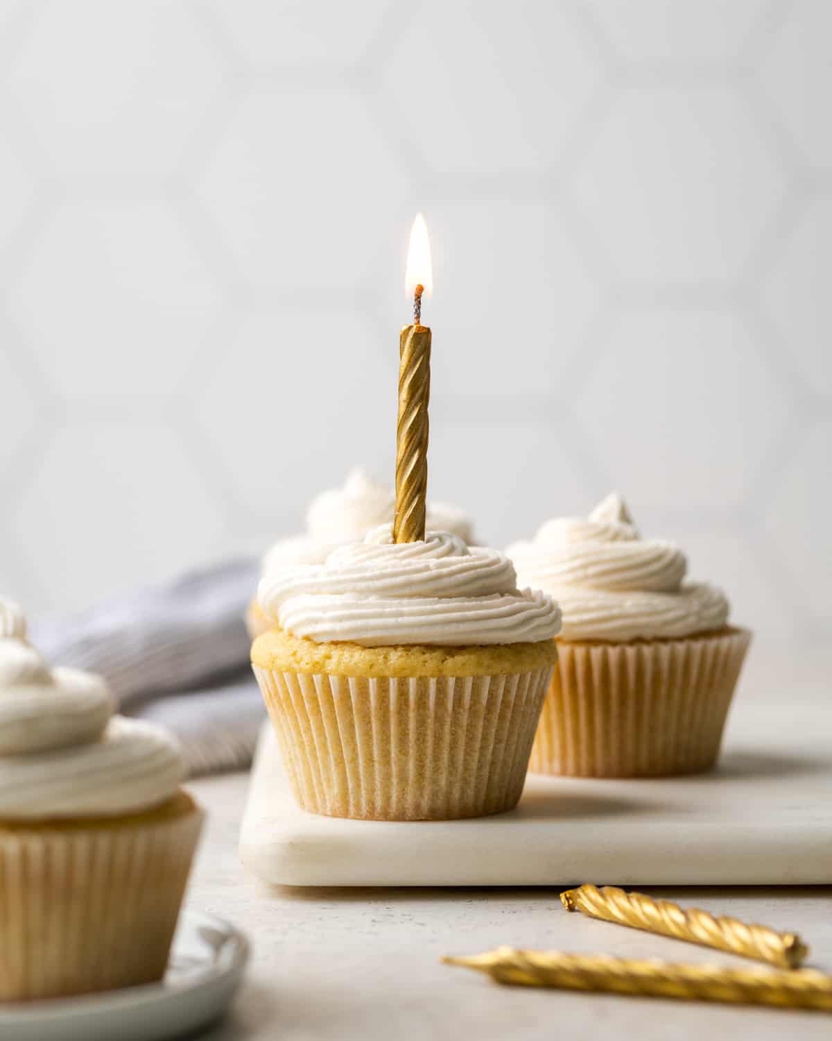 Gluten free vanilla cupcakes topped with vanilla buttercream frosting and gold candles.