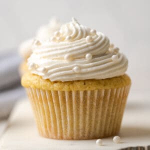 A closeup of a gluten free vanilla cupcake topped with vanilla buttercream frosting and white sprinkles.