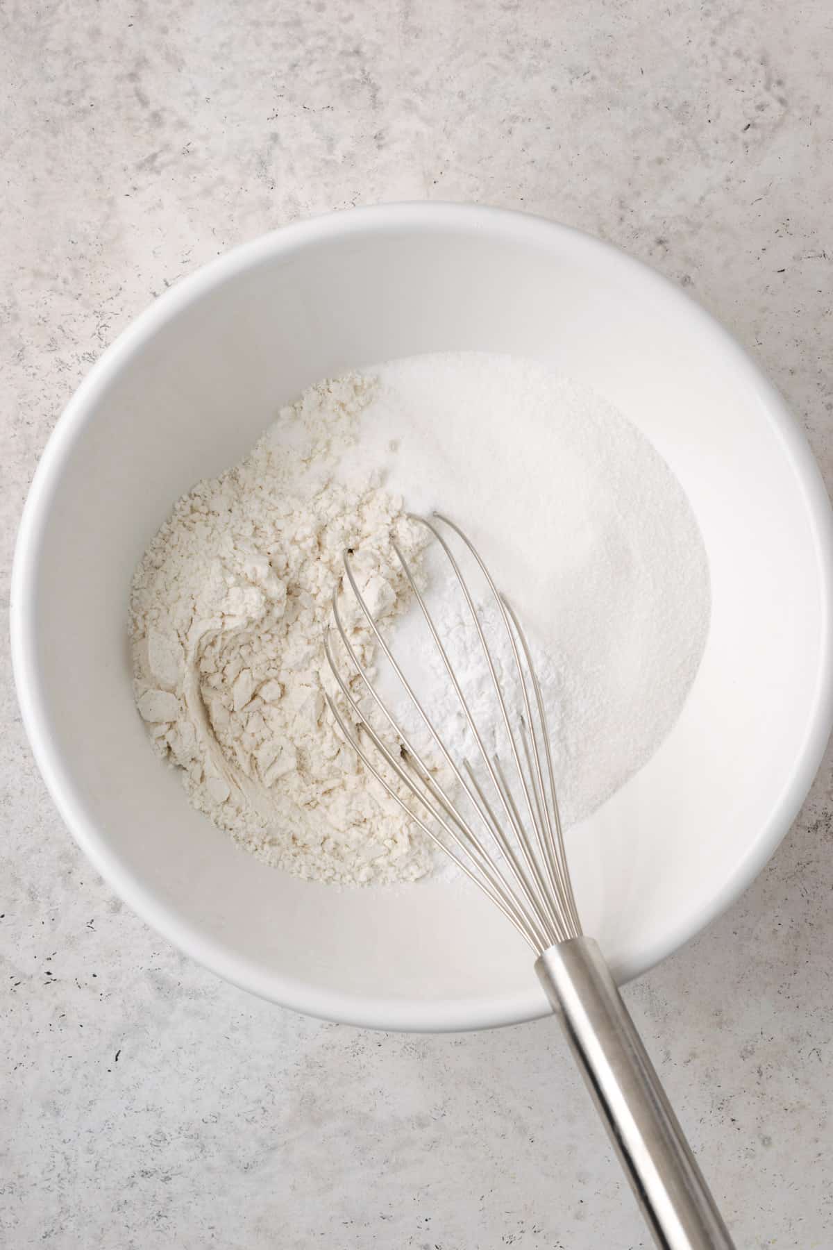 Flour, baking powder, salt and sugar being whisked together in a large white bowl.