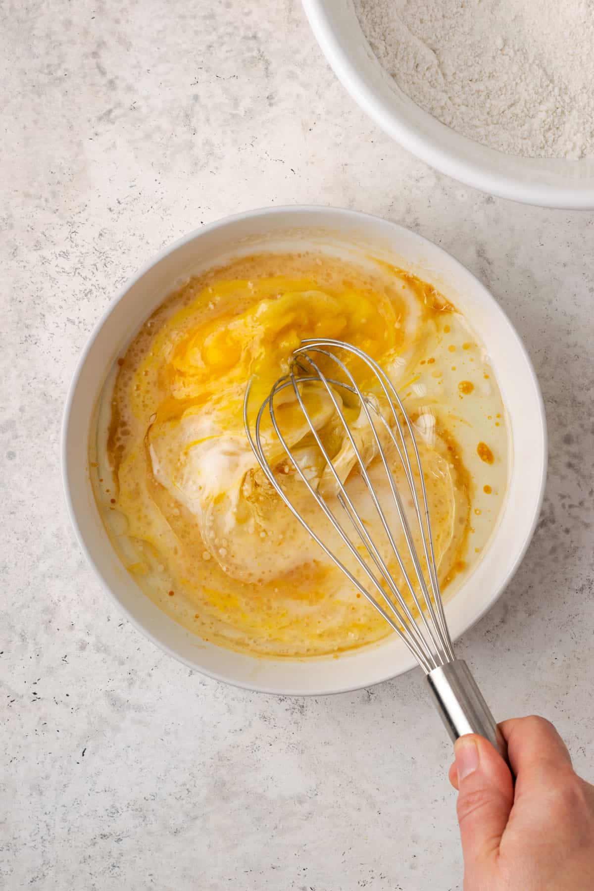 A second bowl with eggs, oil, dairy free milk and vanilla being whisked together.