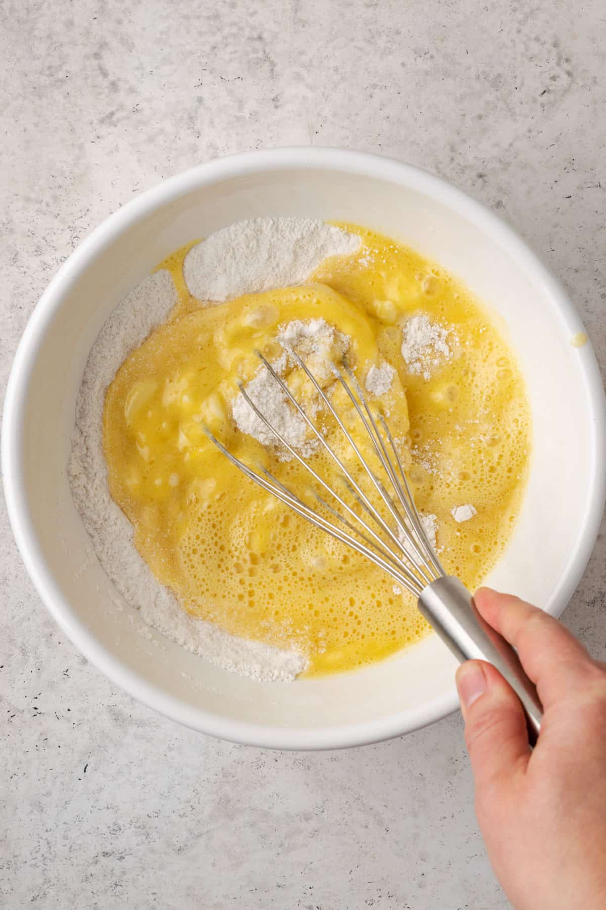 The wet ingredients being mixed into the dry ingredients in a large white bowl.