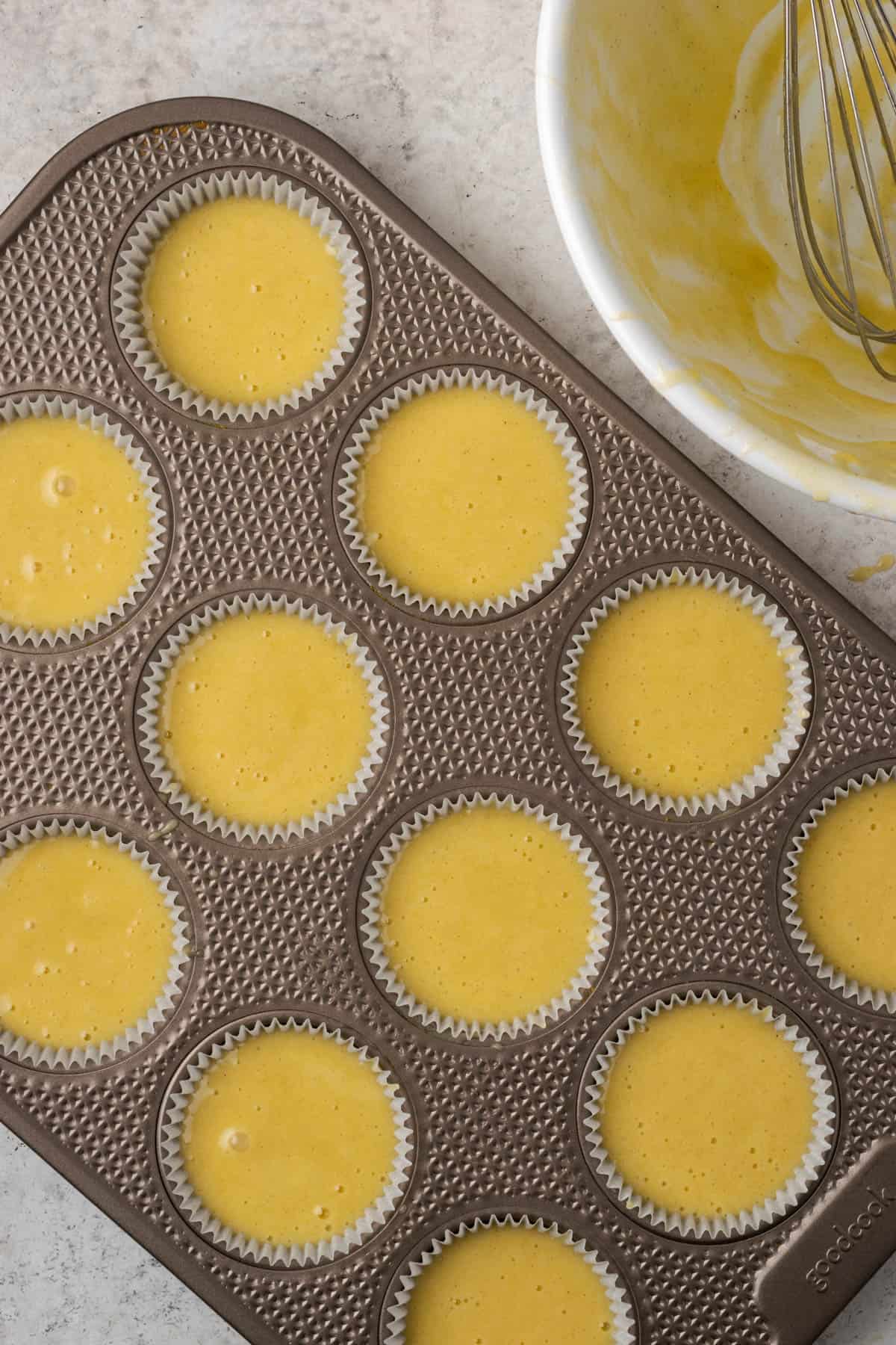 A 12 cup muffin pan lined with paper liners and filled with cupcake batter.