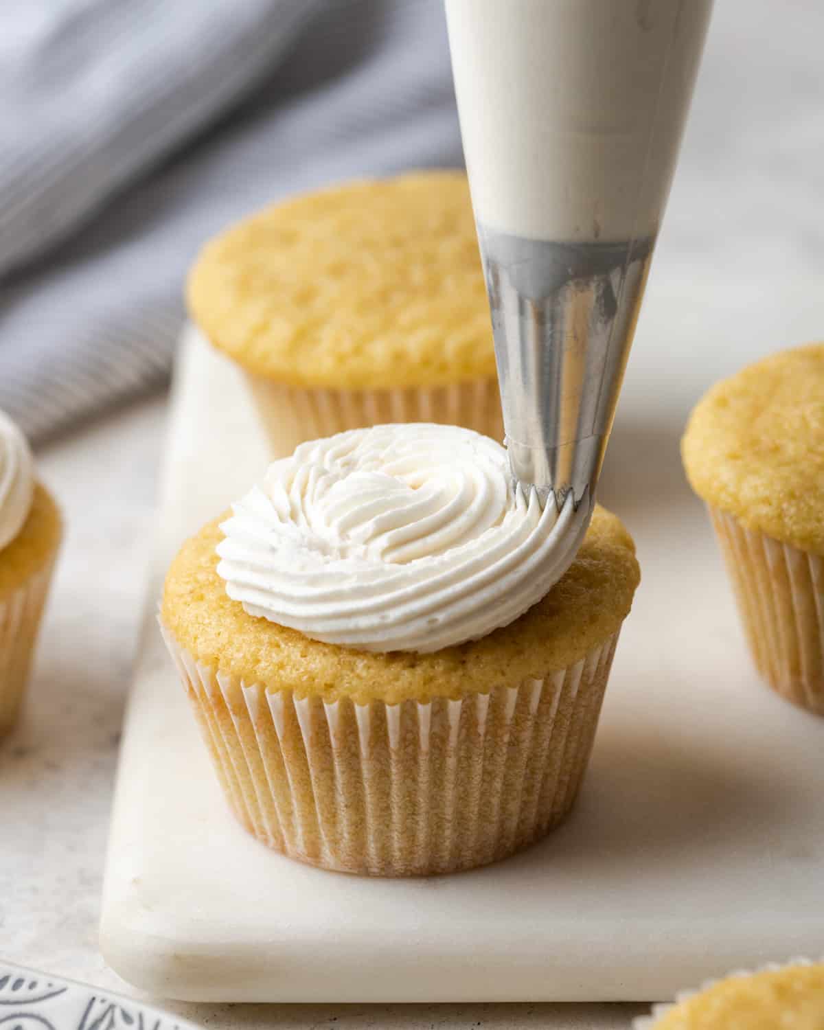 Vanilla buttercream frosting being piped onto a vanilla cupcake with a star tip piping bag.