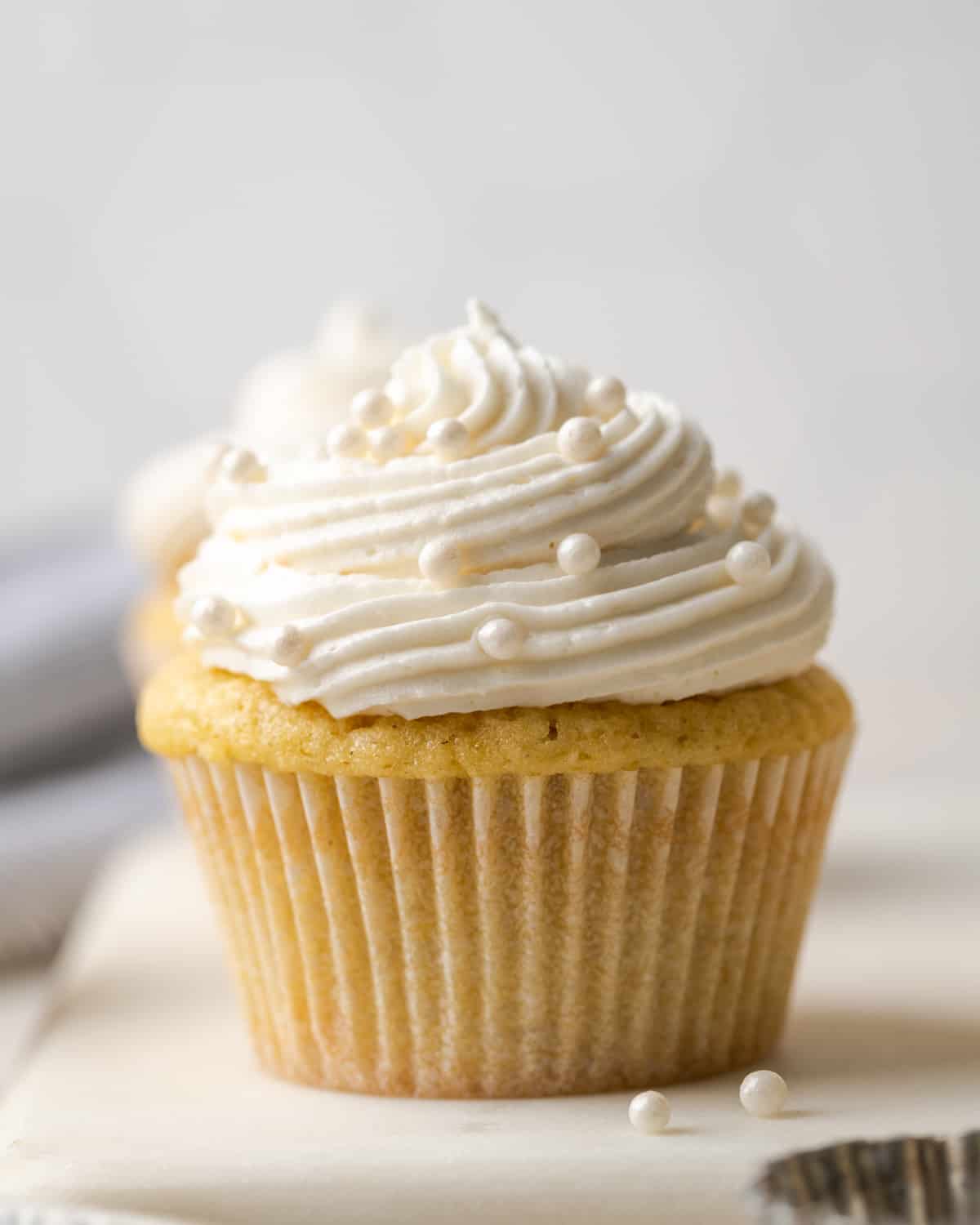 A closeup of a vanilla cupcake topped with dairy free buttercream frosting and white sprinkles.