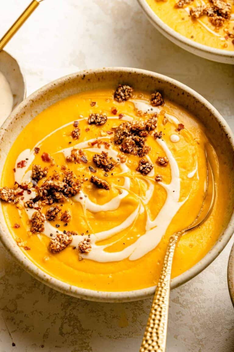 A bowl of sweet potato and carrot soup topped with a swirl of tahini and sesame brittle.