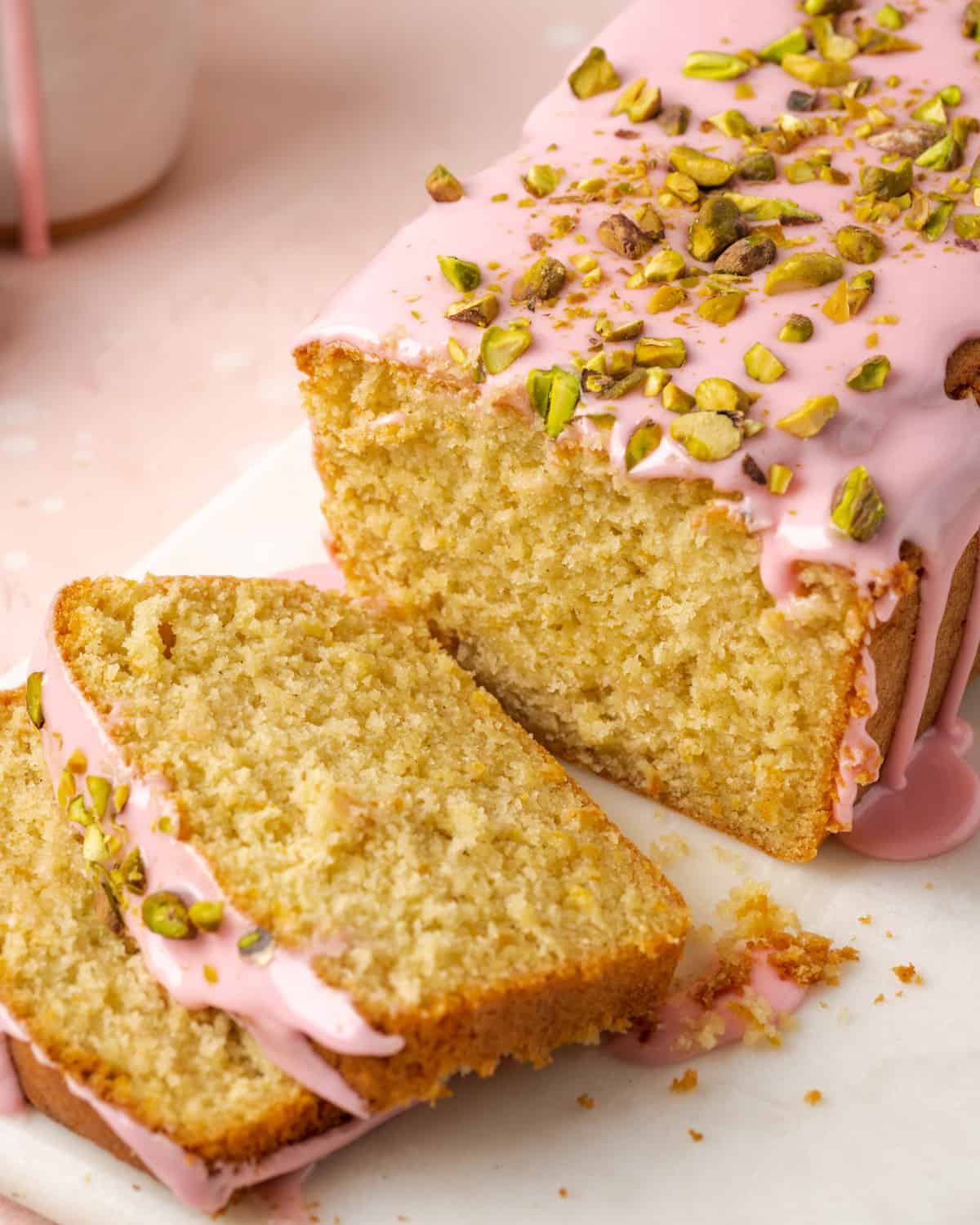 A sliced blood orange pound cake topped with pink icing and chopped pistachios.