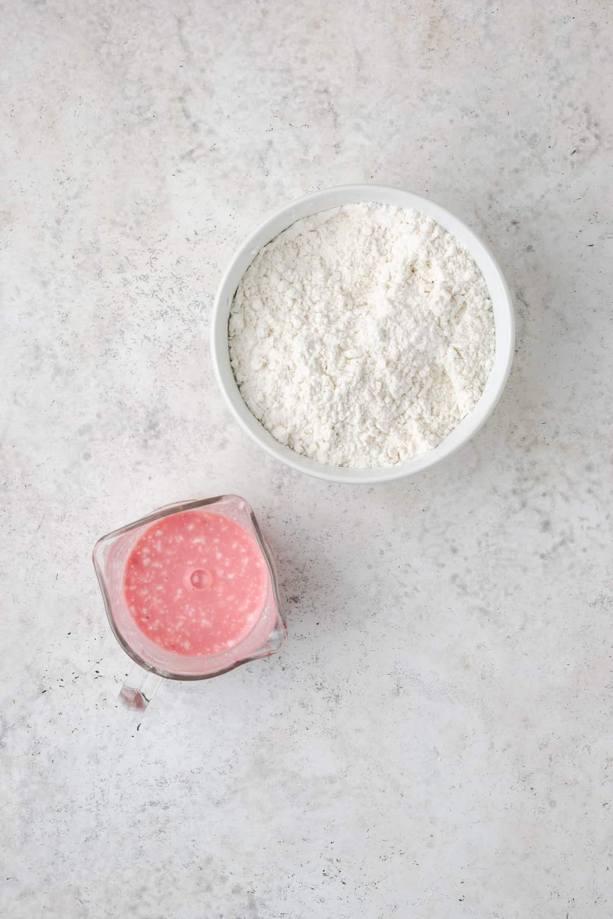 Sour cream mixed with blood orange juice next to a bowl of flour on a white table.