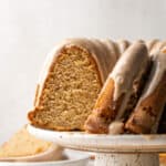 A gluten free banana cake sliced and sitting on a white cake stand.