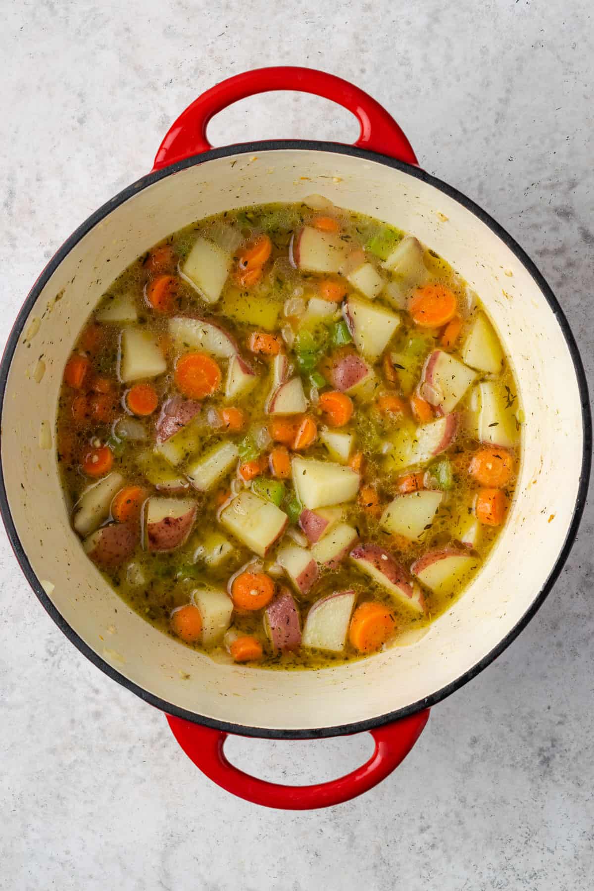 A large pot with partially cooked vegetables and chicken broth.