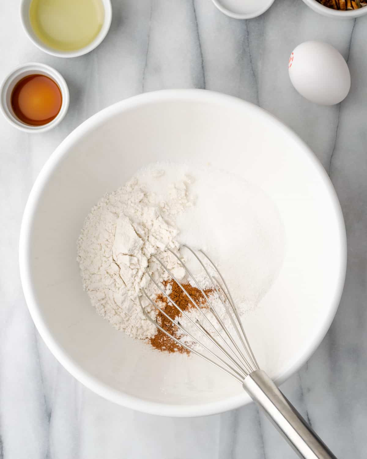 Gluten free flour, baking powder, cinnamon, nutmeg, salt and sugar being whisked together in a large white bowl.