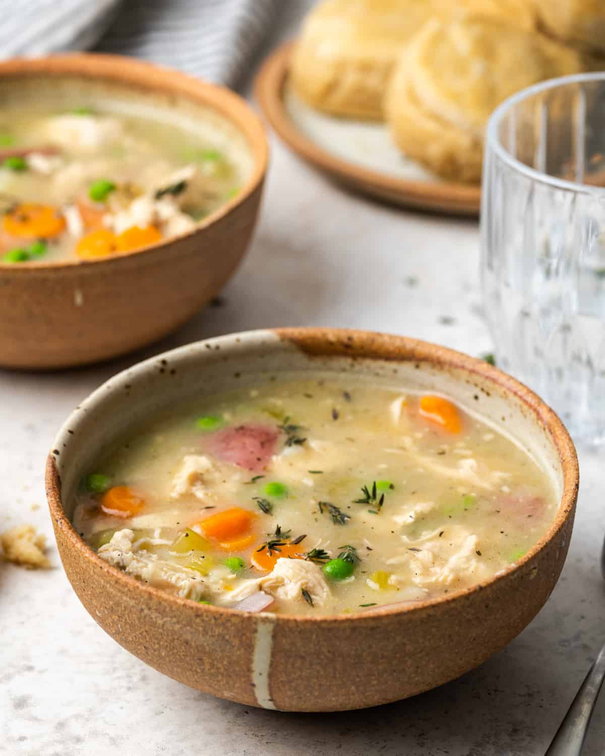 Two rustic bowls filled with chicken pot pie soup with a plate of biscuits in the background.