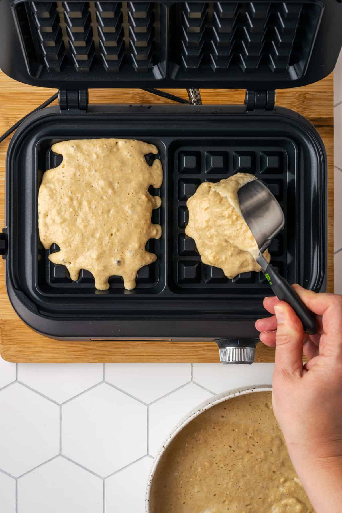 Oat flour waffle batter being scooped into a hot waffle iron.