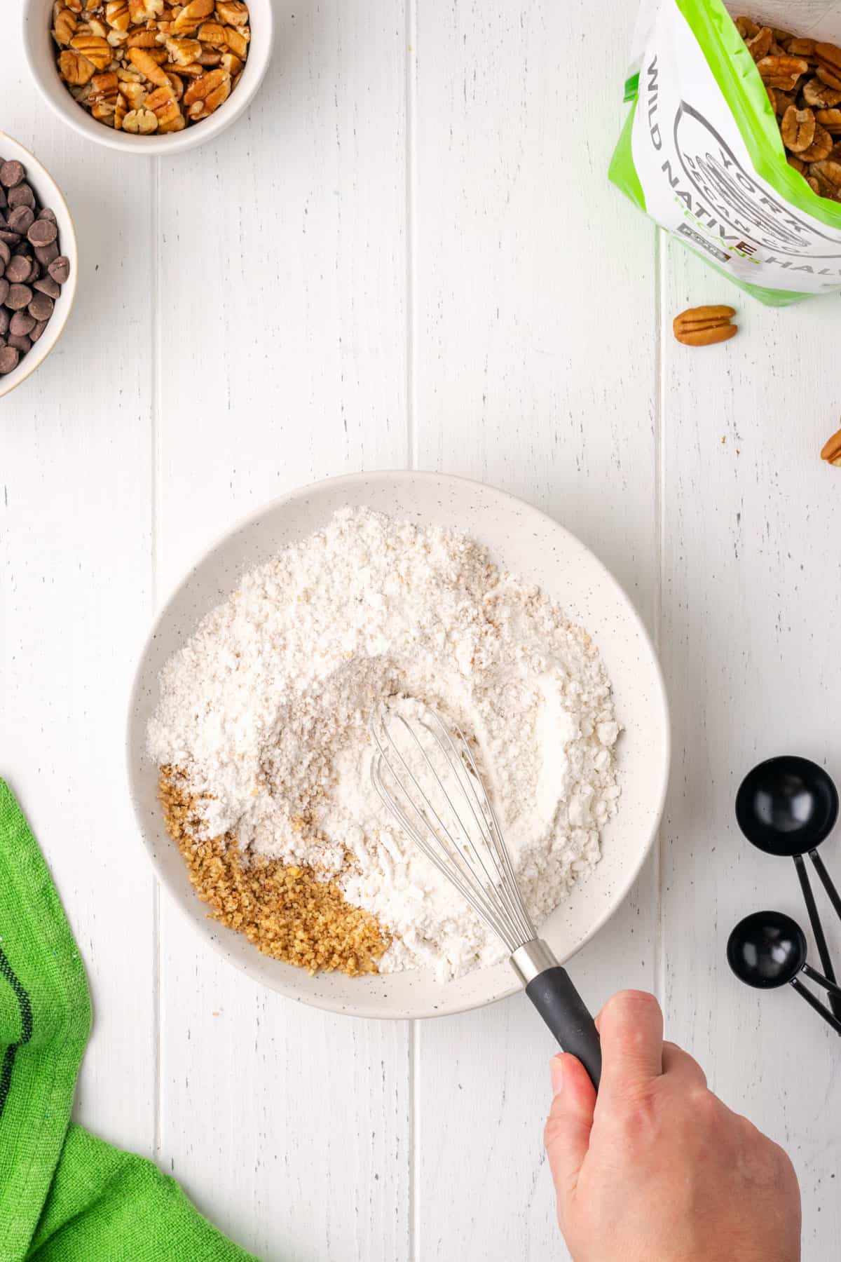 Flour, pecan flour, baking soda, baking powder, cinnamon, cayenne pepper and salt being whisked together in a small white bowl.