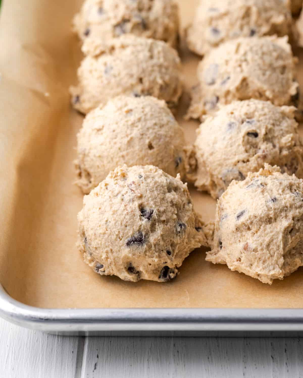 Balls of pecan chocolate chip cookie dough lined up on a parchment lined baking sheet.