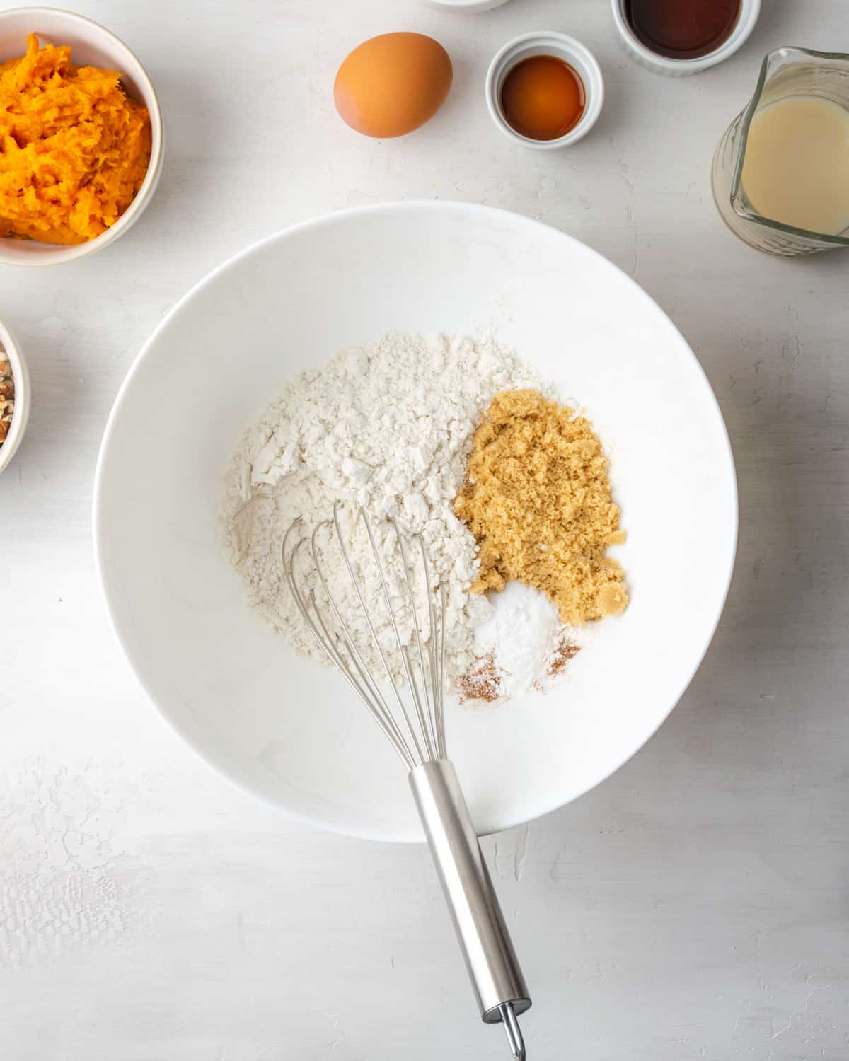 Flour, baking powder, baking soda, cinnamon, nutmeg, salt and brown sugar combined together in a large white mixing bowl.