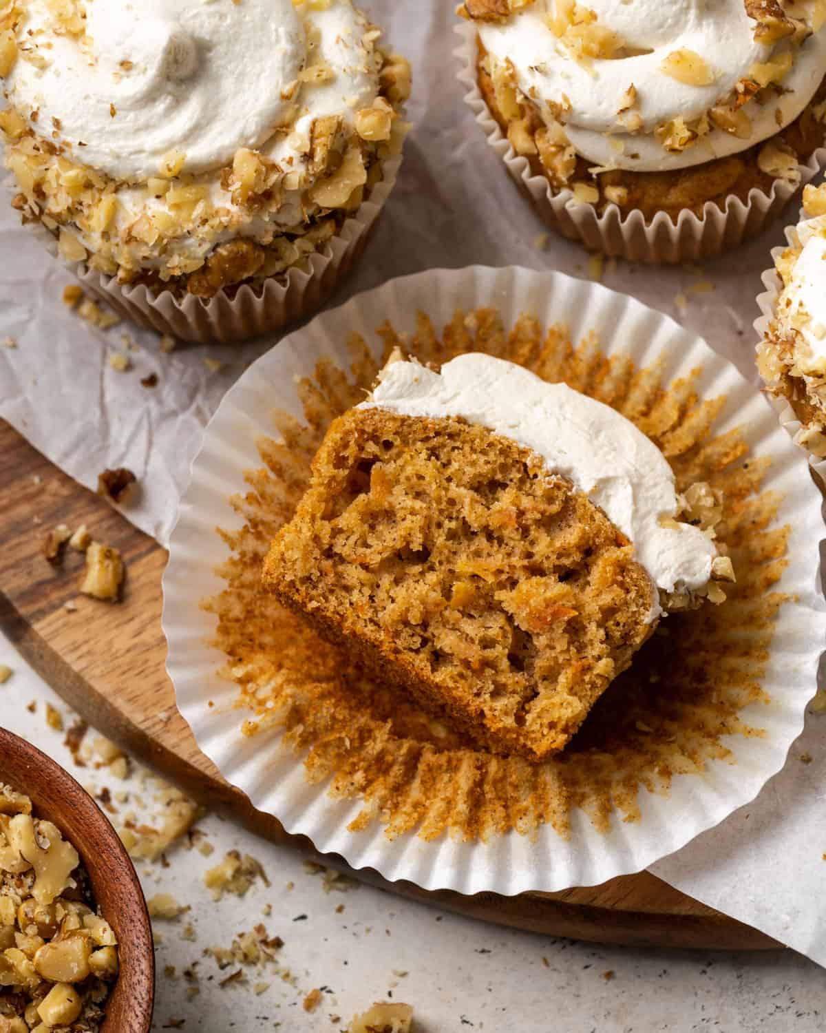 Carrot cake cupcake cut in half and laying on a wooden cutting board.