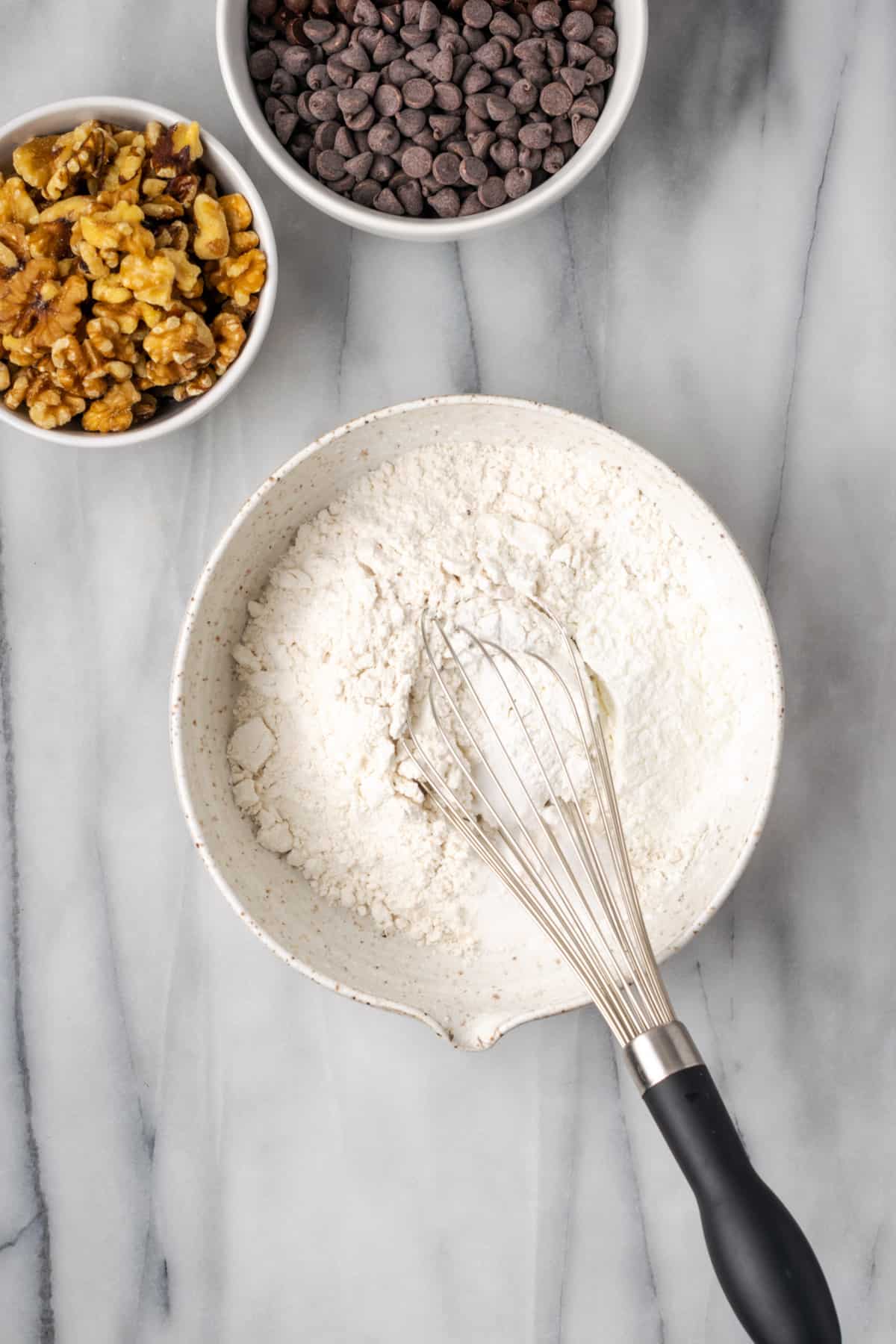 Gluten free flour, cornstarch, baking powder, baking soda and salt being whisked together in a white bowl.