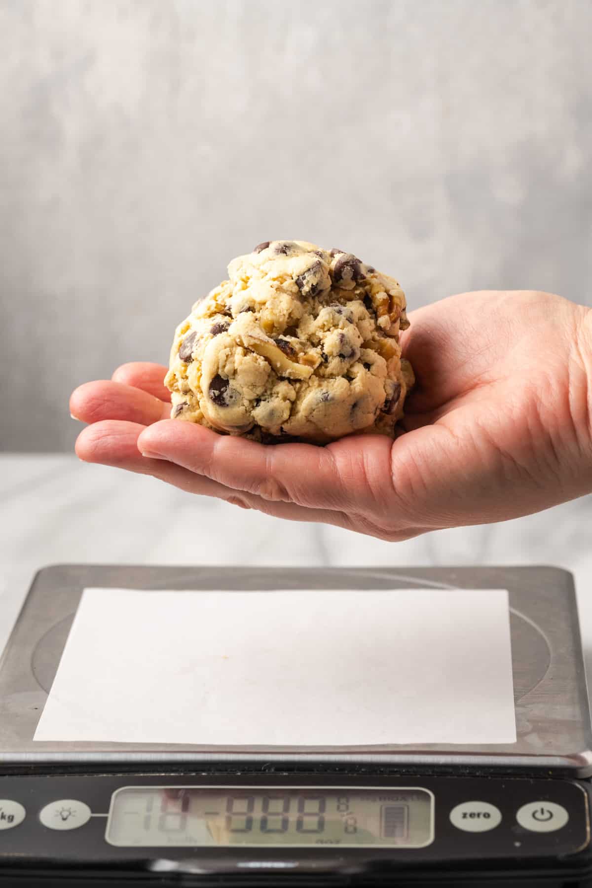 A huge ball of cookie dough being held in the palm of a hand.