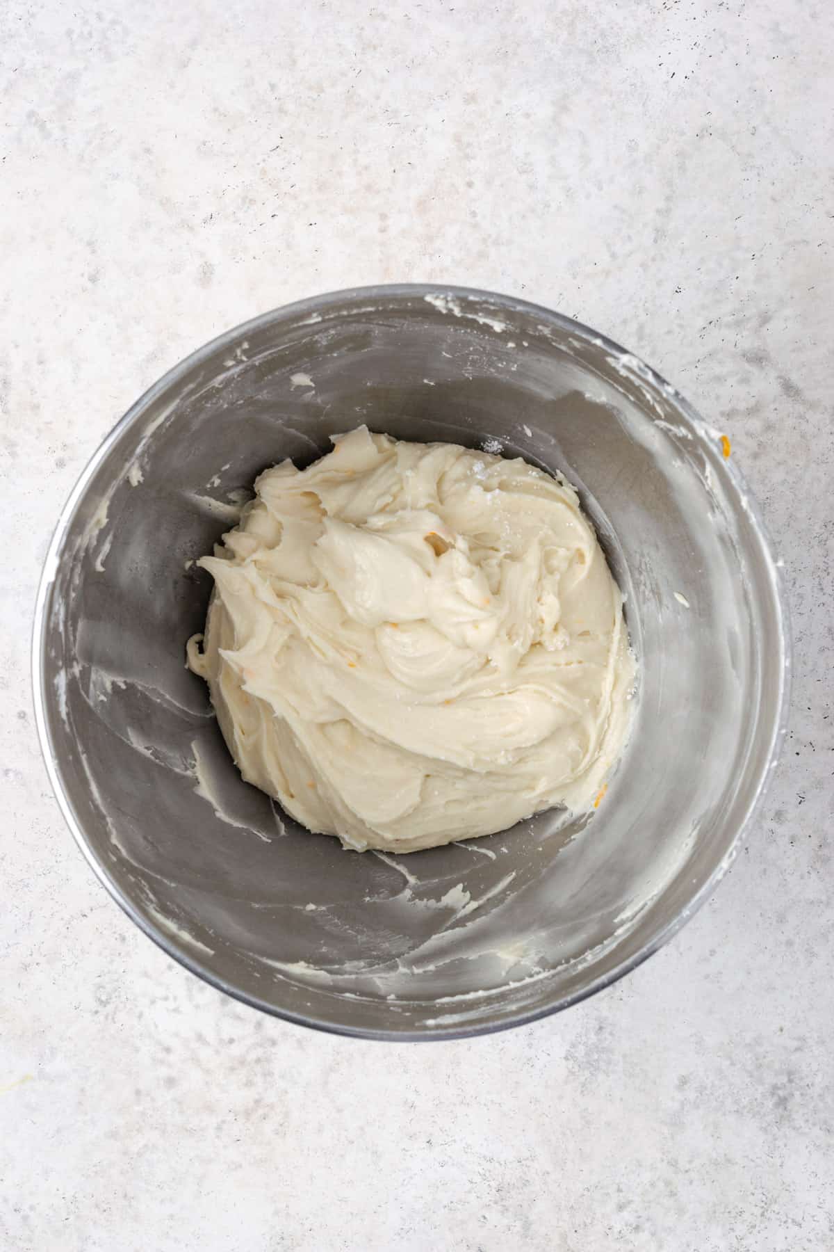 Orange cream cheese frosting in a large metal mixing bowl.