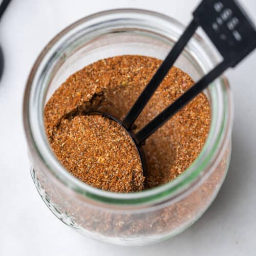 A jar filled with homemade taco seasoning and a scoop.