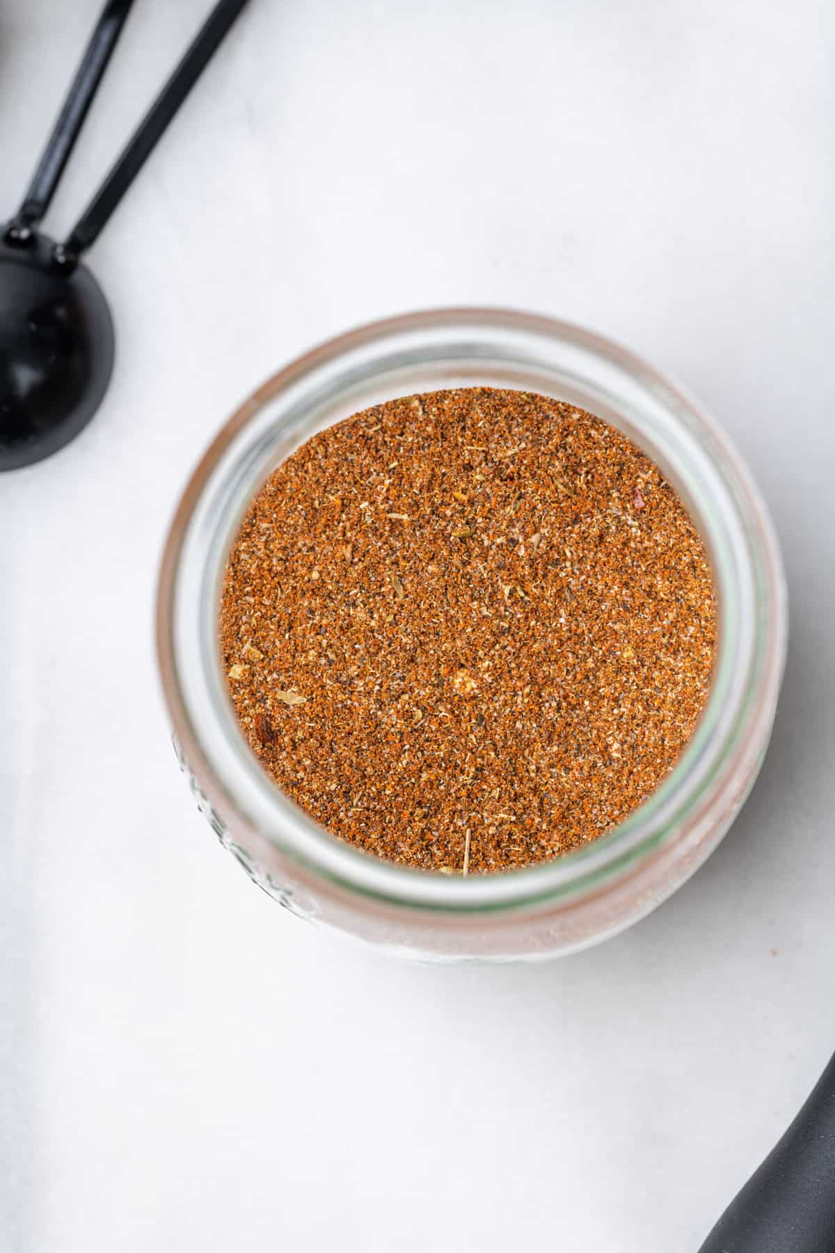A jar filled with homemade taco seasoning on a white table.