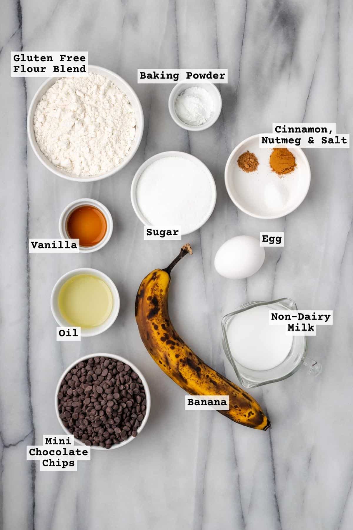 Ingredients for chocolate chip banana muffins on a white marble table.