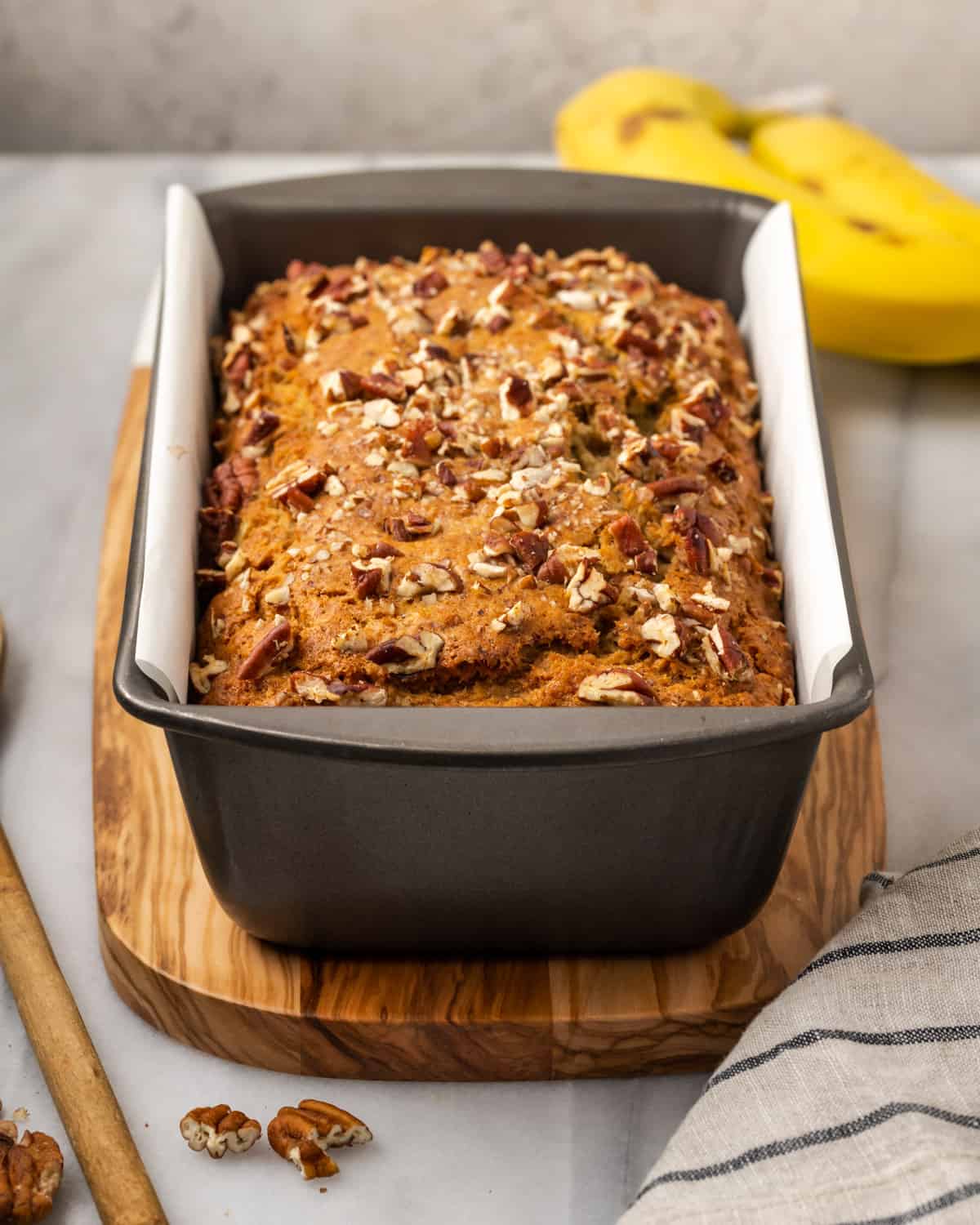 A freshly baked loaf of banana bread topped with pecans in a metal baking tin.