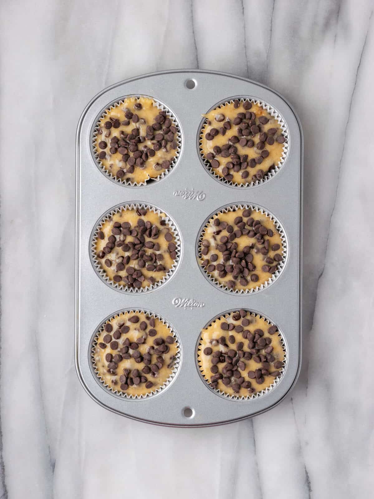 Unbaked banana chocolate chip muffins in a 6 cup muffin tin.