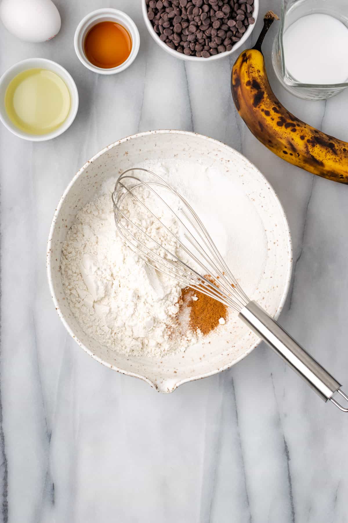 Gluten free flour, sugar, baking powder and spices being whisked together in a large white mixing bowl.