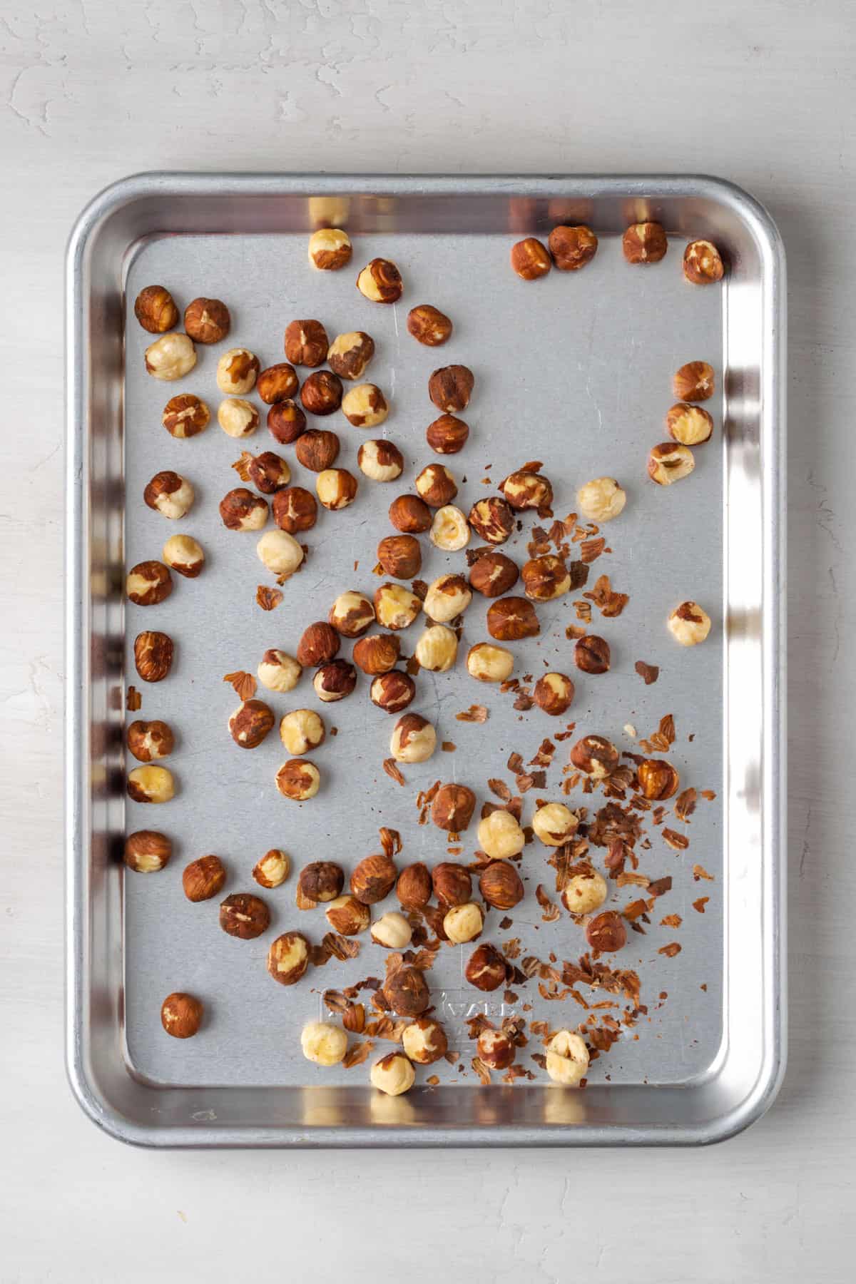 Raw hazelnuts on a metal baking tray.