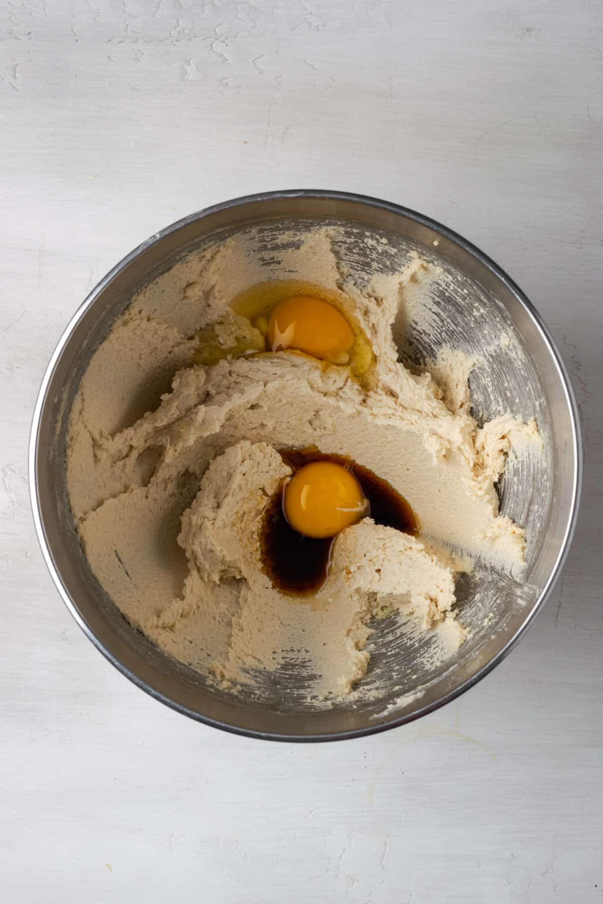 An egg, egg yolk and vanilla added to the creamed butter and sugar mixture in a metal mixing bowl.