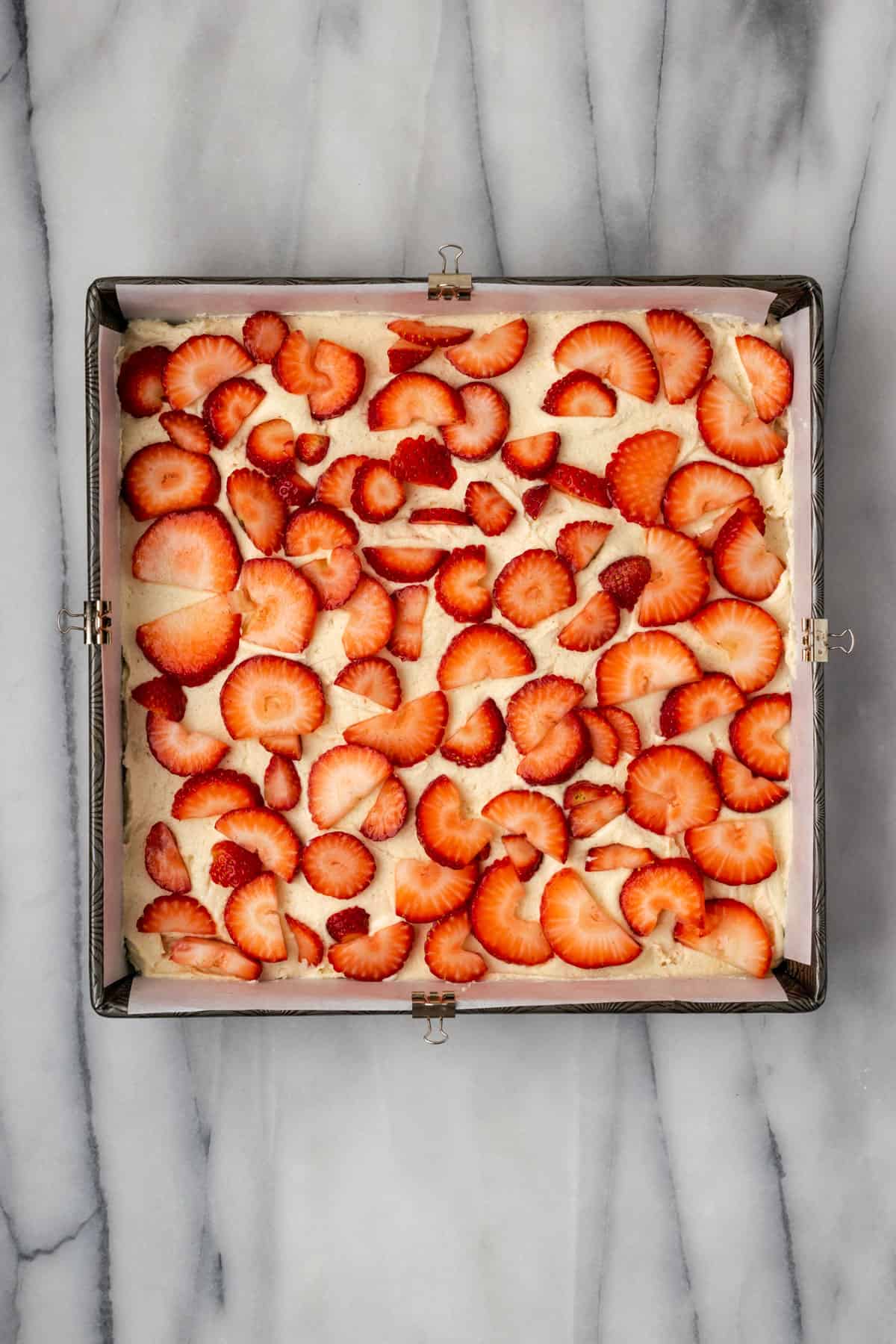 Strawberries spread on top of cake batter in a square baking pan.
