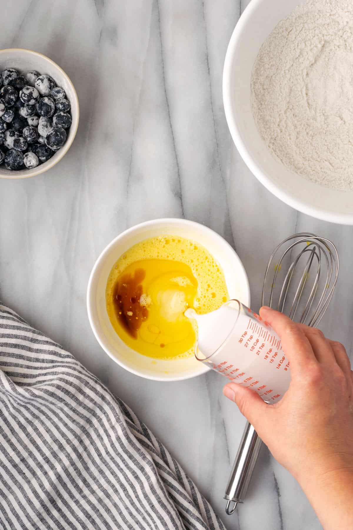 Oil, vanilla and milk being poured into the whisked egg. 