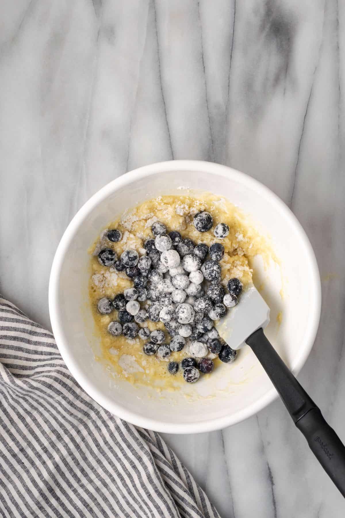 Flour coated blueberries being added to the bowl of muffin batter.