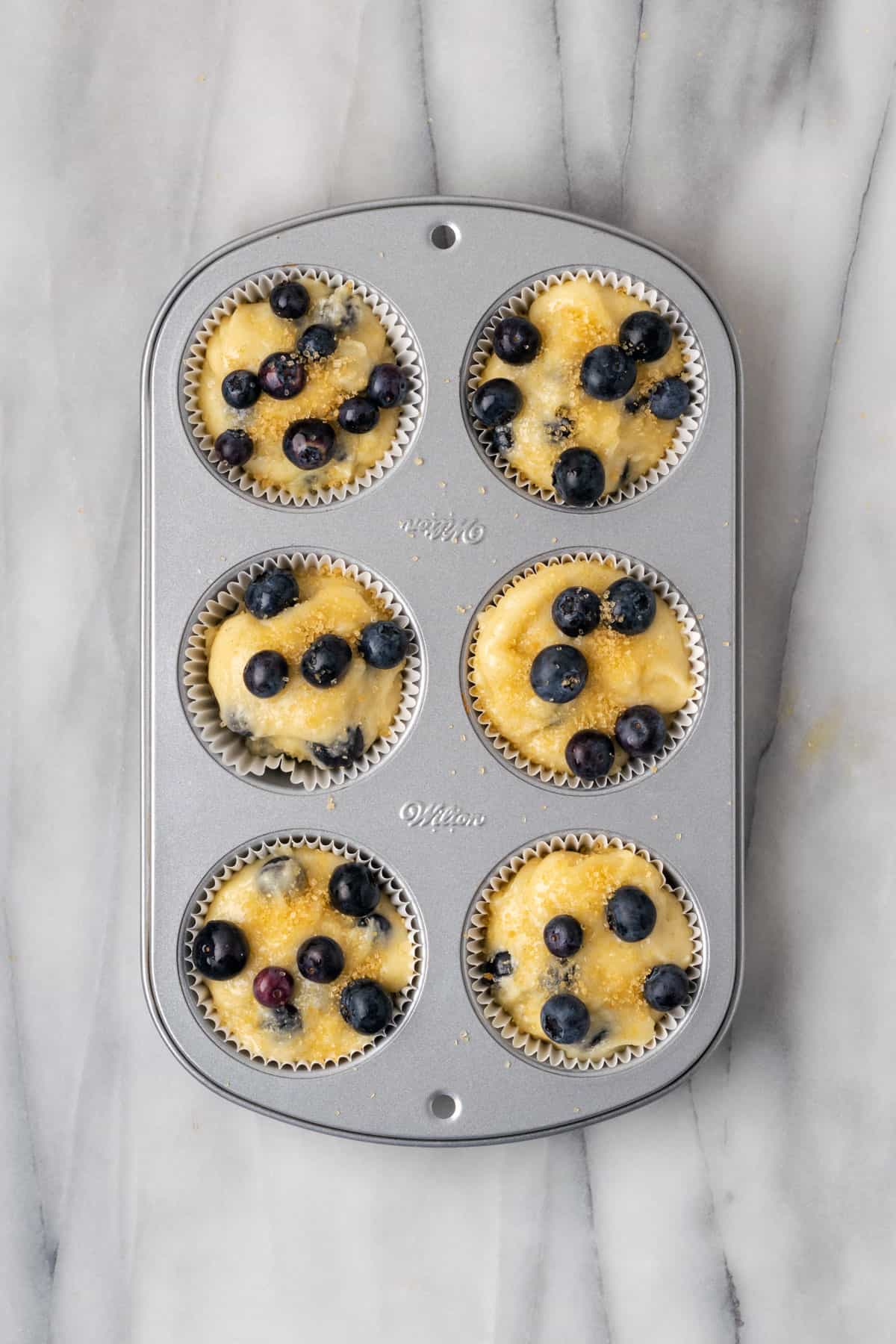 A muffin tray filled with unbaked blueberry muffin batter.