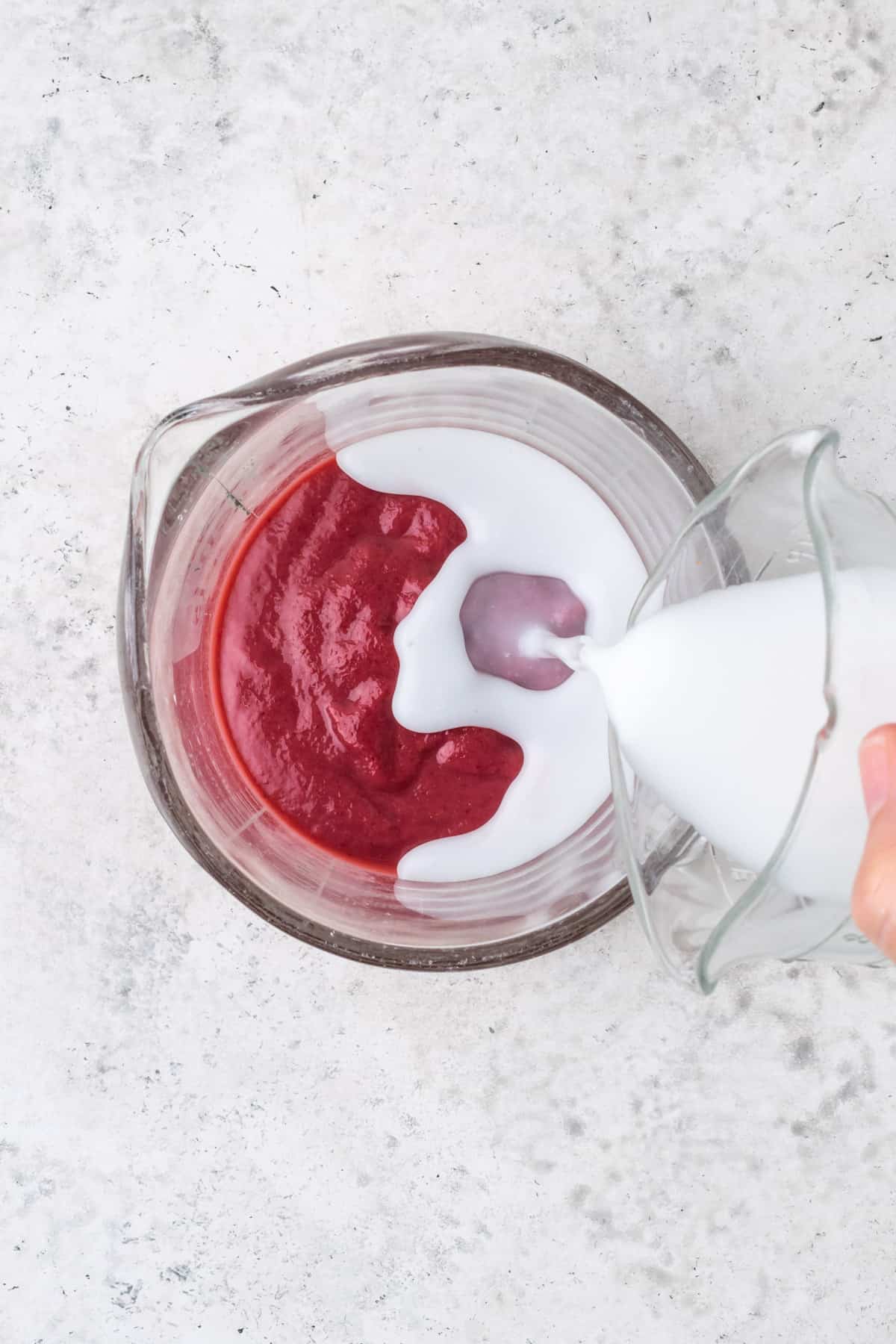 Milk being poured into a glass measuring cup holding the strawberry puree.